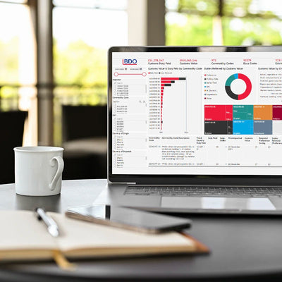 A laptop displaying a customisable data analytics dashboard, with a cup of coffee and a notebook beside it, set on a table in a well-lit room.